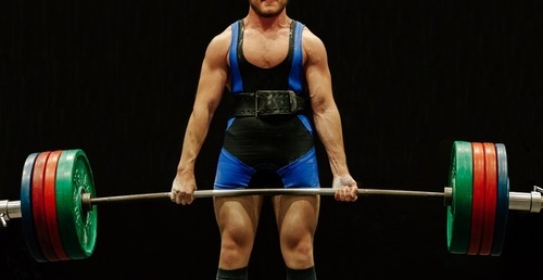 A strong male powerlifter performing a heavy deadlift with a weighted barbell and lifting belt.