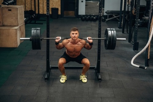 Muscular man performing a heavy barbell back squat in a gym setting for strength training.