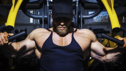Muscular male bodybuilder performing a chest press on a yellow gym machine for strength training.