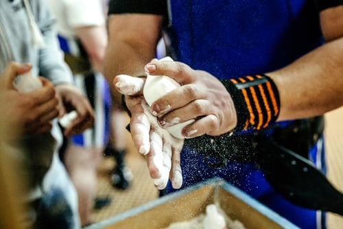 Weightlifter applying white lifting chalk to hands for better grip during a powerlifting workout.