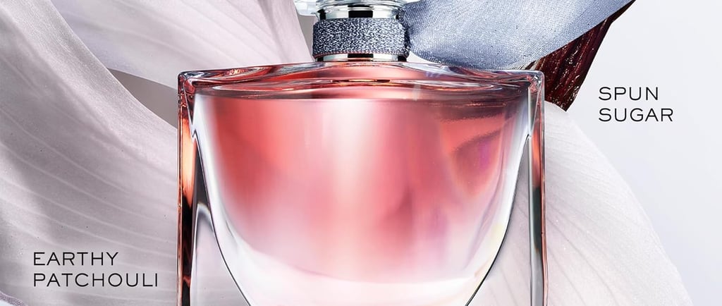 A pink perfume bottle with a clear square cap is surrounded by light purple iris petals, green leave