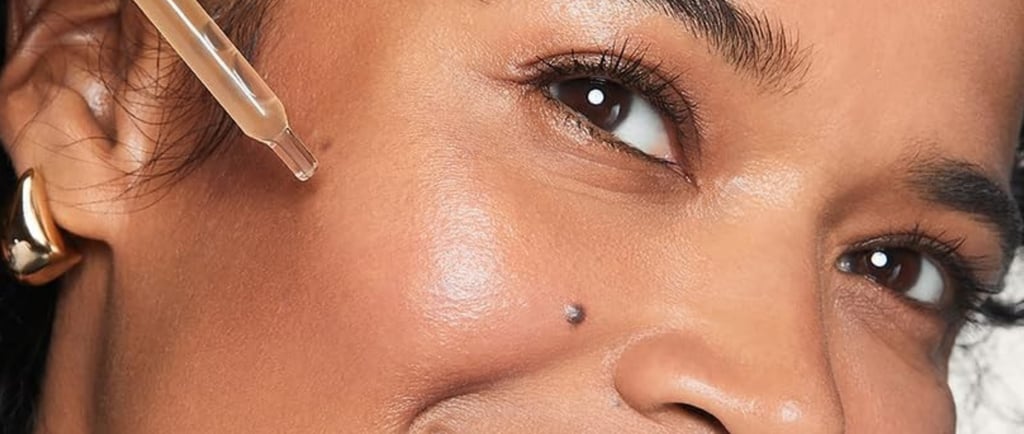 Smiling woman holds a dropper near her cheek, showcasing glowing, moisturized skin.