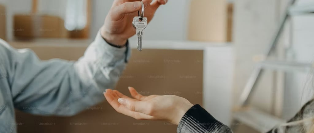 A person handing house keys to a new homeowner with moving boxes in the background.