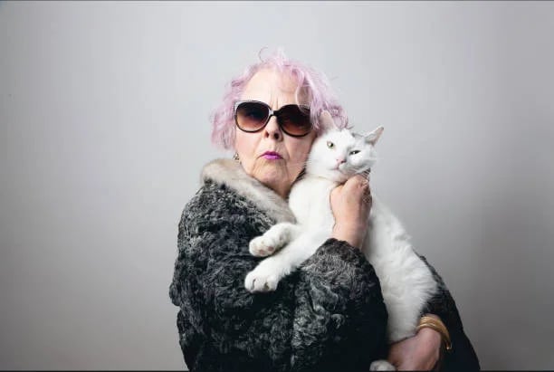 femme agée serrant contre elle son chat blanc avec son manteau de fourrure et portant des lunettes d