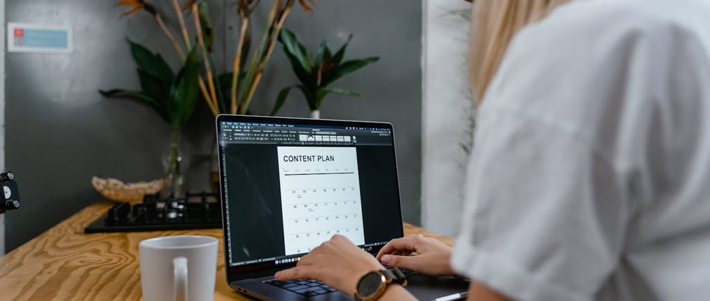 A woman sat on a chair working on her laptop with a cup of coffee by her side
