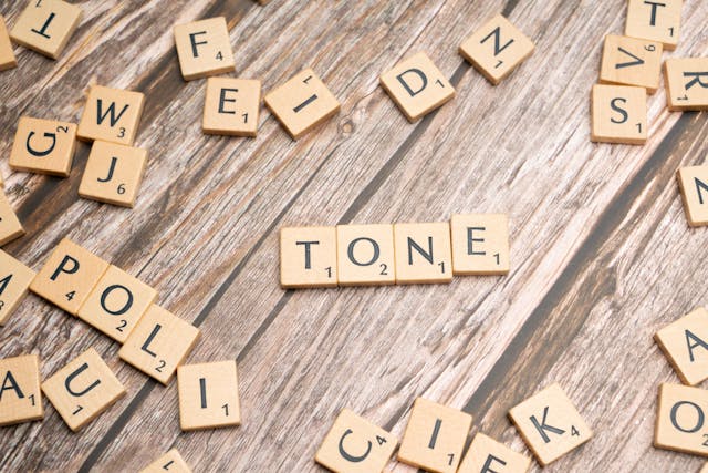 Scrabble pieces laid out on a table spelling the word "tone"