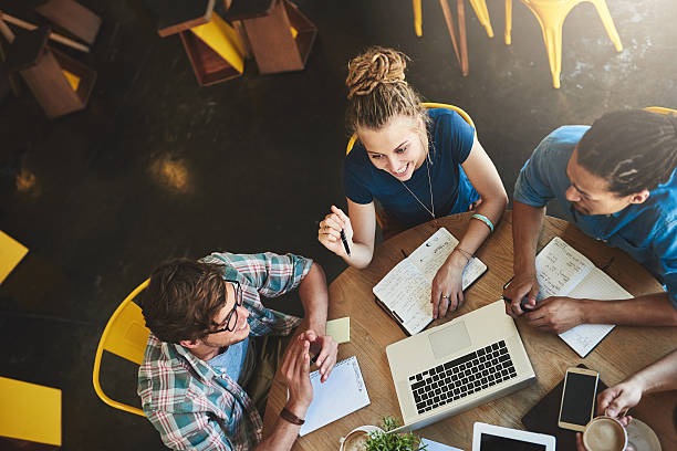 Overhead shot of three smiling university students studying together at a coffee shop table, with a 