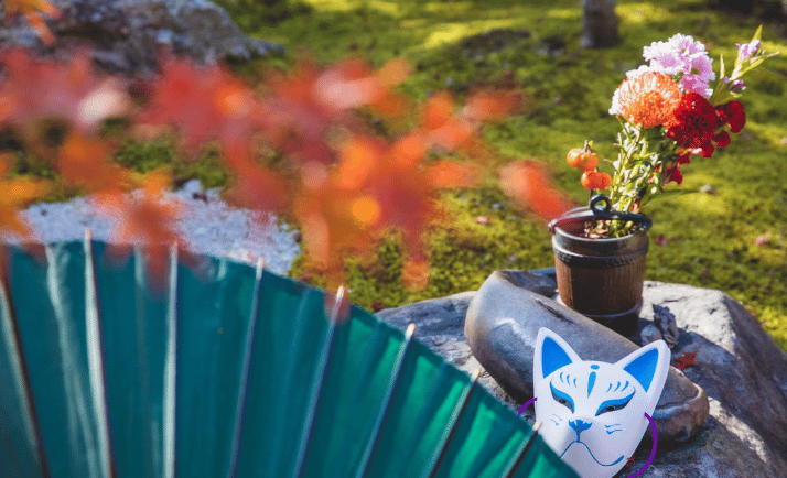 Arranjo de flores coloridas ao ar livre em jardim zen com máscara kitsune e elementos decorativos ja
