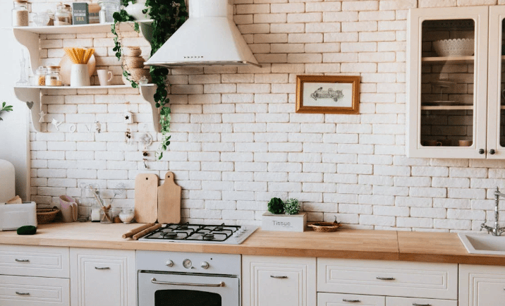 Cozinha clara com armários brancos, bancada de madeira e decoração com plantas e utensílios