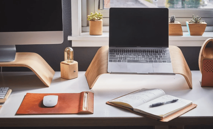 Home office compacto com suporte para notebook, caderno e decoração com plantas.
