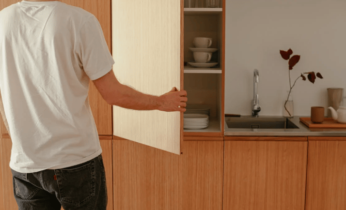 Homem abrindo armário de cozinha planejada em ambiente minimalista com madeira clara.