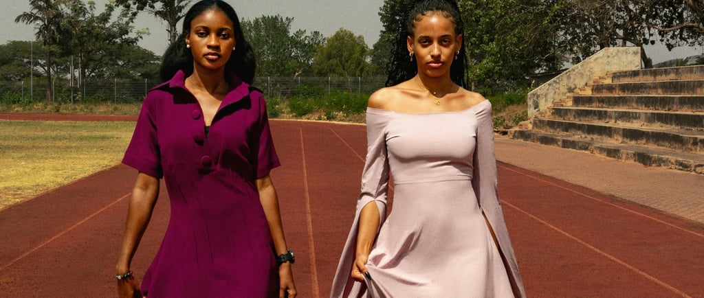 Two women in elegant evening gowns walking on a red running track at an outdoor stadium.