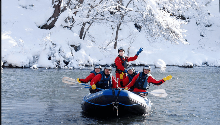 A group of happy people enjoying winter whitewater rafting on a river surrounded by snow-covered trees.