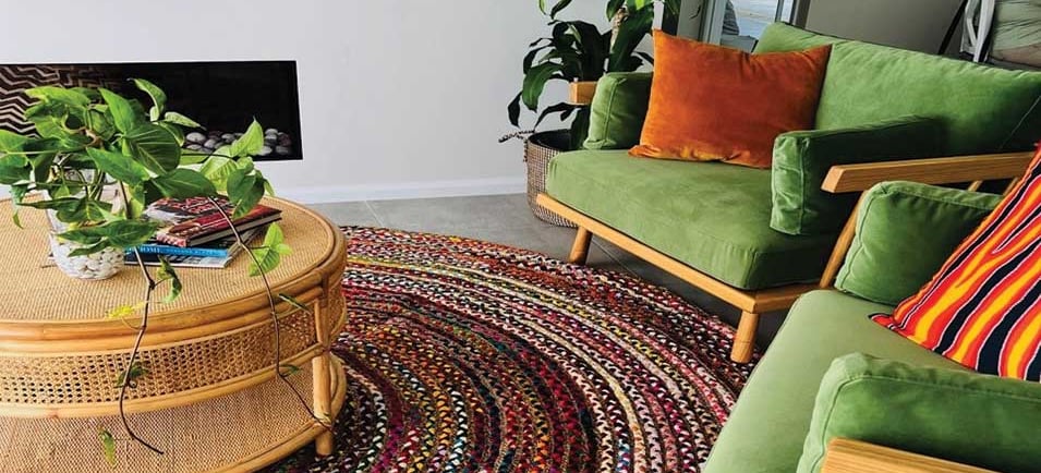 a living room with a green couch and a table with a potted plant and jute fabric carpet
