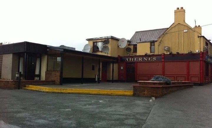 Exterior view of Aherne's pub in Tallaght with a red frontage and outdoor seating area.