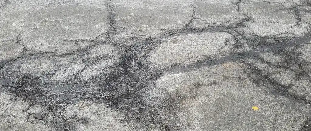 Worn asphalt surface showing winter damage from snow plows, salt, and freeze thaw cycles affecting 