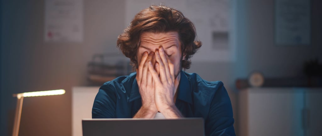 Person sitting at a laptop with hands covering face, showing frustration during a job search.
