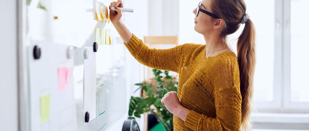 Woman writing on sticky notes on a whiteboard, representing planning and organization.