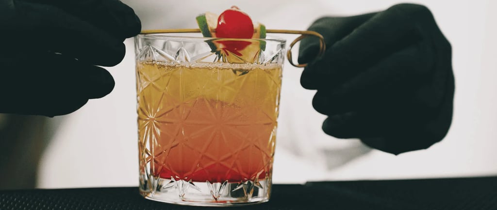 Bartender in black gloves garnishing a craft tequila sunrise cocktail with a cherry and lime.