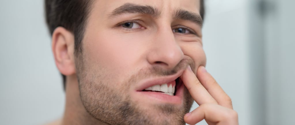 A man examining his red, inflamed gums in a mirror to check for signs of gingivitis or dental pain.