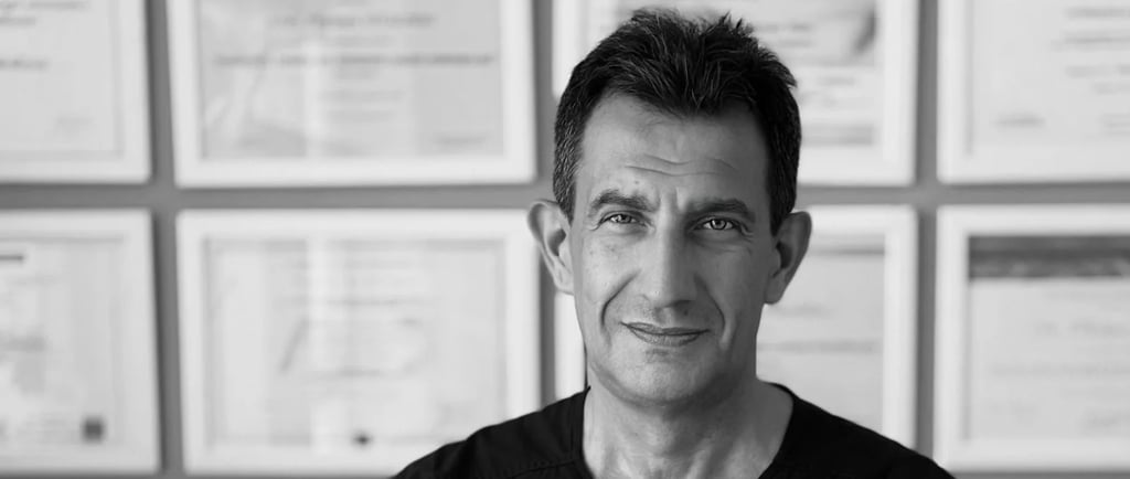 Portrait of professional dentist Dr. Pierluca Vidini in medical scrubs with dental certifications on the wall.