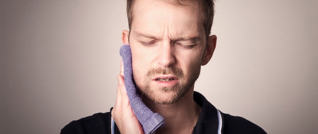 A man holding a purple washcloth to his face to relieve severe toothache and jaw pain.
