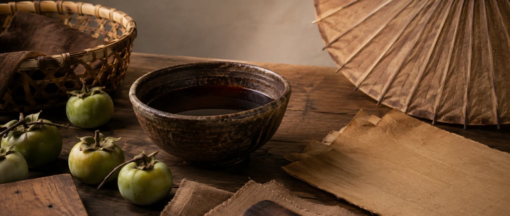 Traditional ceramic tea bowl with green persimmons and a paper umbrella on a rustic wooden table.