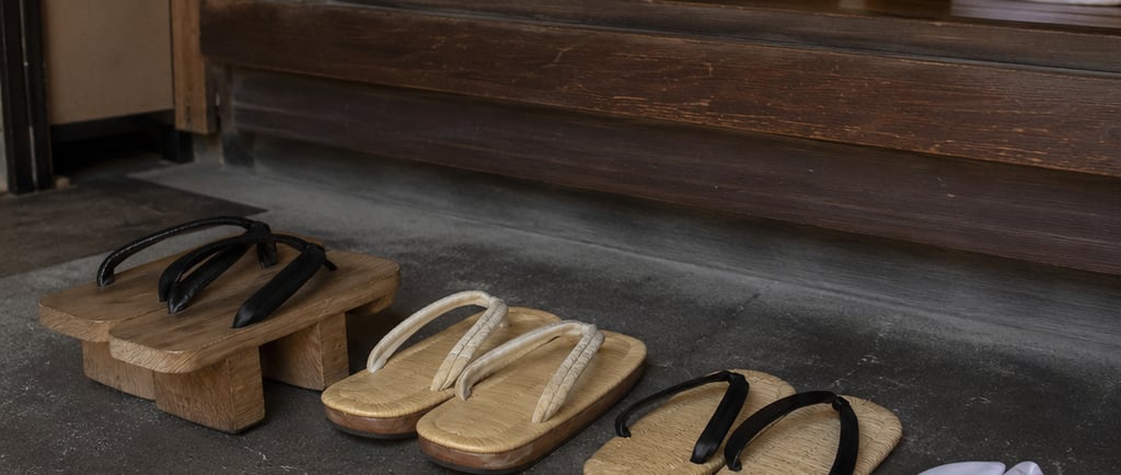 Traditional Japanese wooden geta and straw zori sandals placed at a wooden temple entrance.