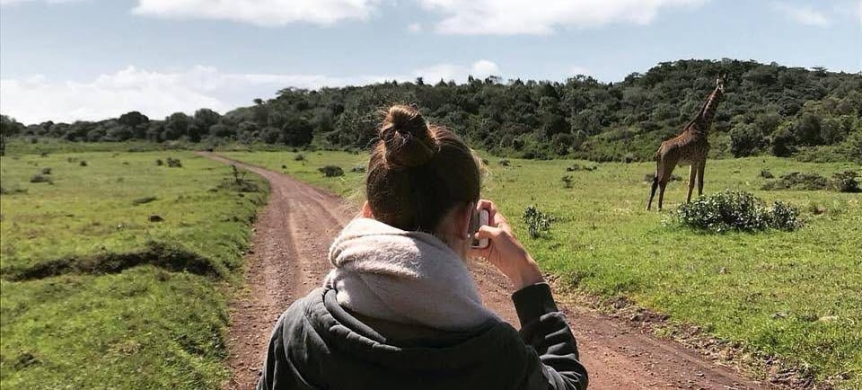 Tourist on a safari trail inside Tarangire National Park holding a camera and photographing a giraffe in its natural wildlife