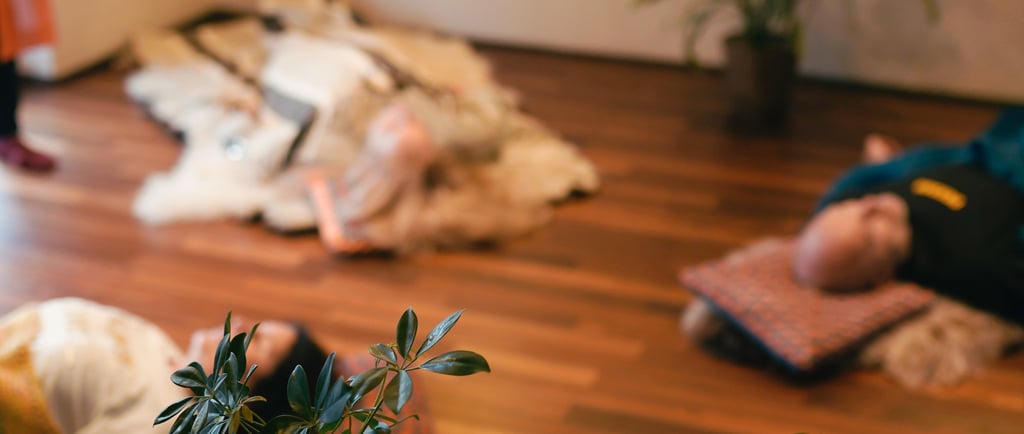 Несколько человек лежат на ковриках и подушках, расслабляясь во время дыхательной практики