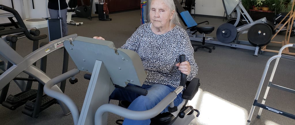 a woman in a gym room with a man on a stationary bike