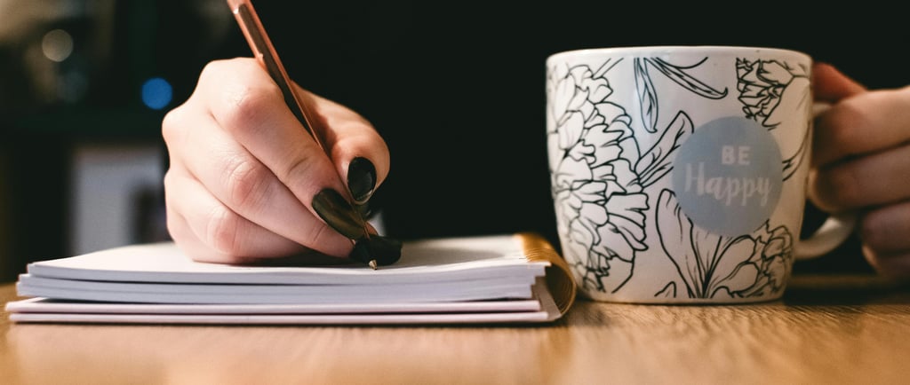 a person writing on a notebook with a cup of coffee