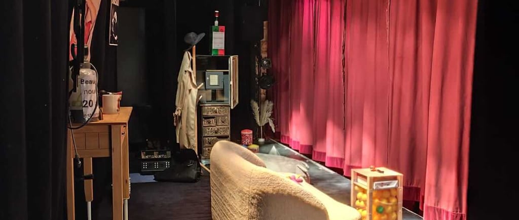 Décor de scène théâtrale : canapé beige tourné vers le fond, table transparente remplie de balles co