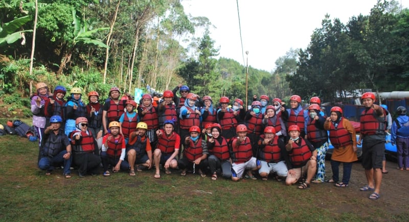 Peserta team building perusahaan sedang berpose mengenakan helm dan jaket pelampung sebelum kegiatan rafting di Bandung.