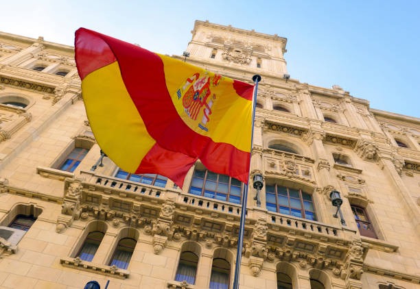 Bandera española delante de un gran edificio amarillo