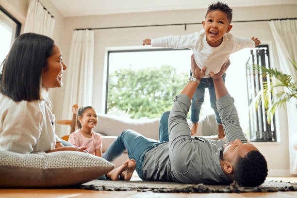 Una familia está jugando en la alfombra, el niño está sostenido en el aire por su padre.