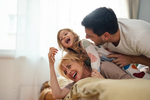 Una familia feliz riendo, madre, padre y una niña entre ellos.