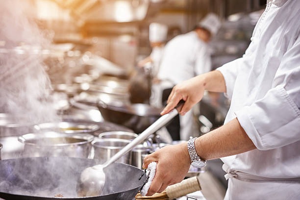 El chef revuelve la comida en una sartén.Lleva un reloj en la muñeca izquierda.