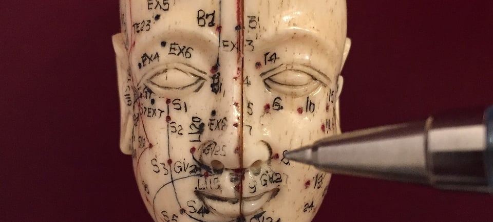 eine asiatische Kopfstatue mit aufgemalten Akupunkturpunkten und Meridianen