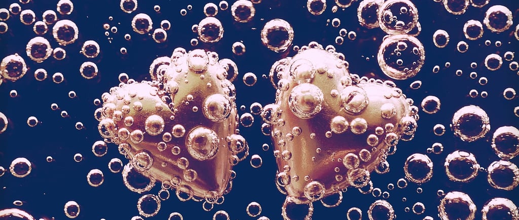 zwei metallene Herzen schwimmen im Wasser und sind von Blasen umgeben