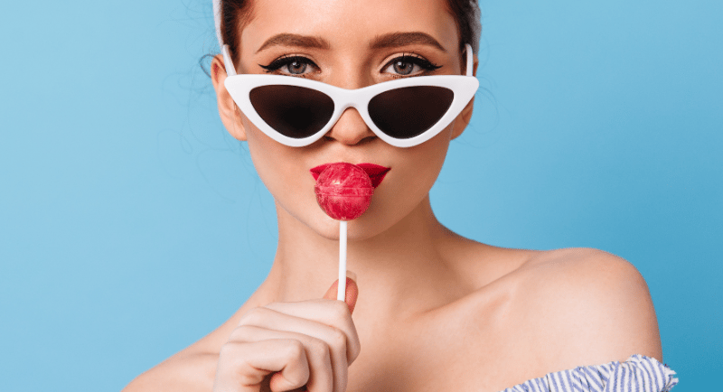 a woman with sunglasses and licking a lollipop
