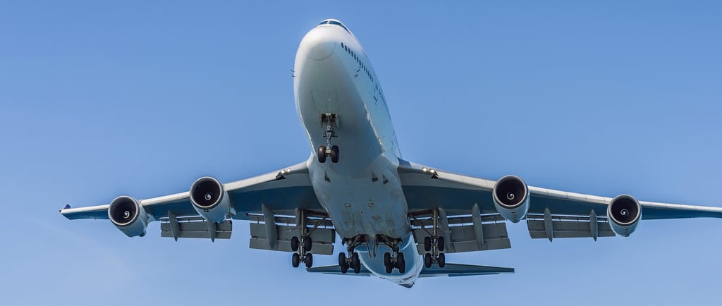 Low-angle view of a Boeing 747 jumbo jet flying in a clear blue sky with landing gear deployed.