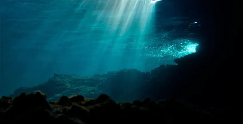 Visão subaquática das profundezas do oceano com raios de sol atravessando a água azul