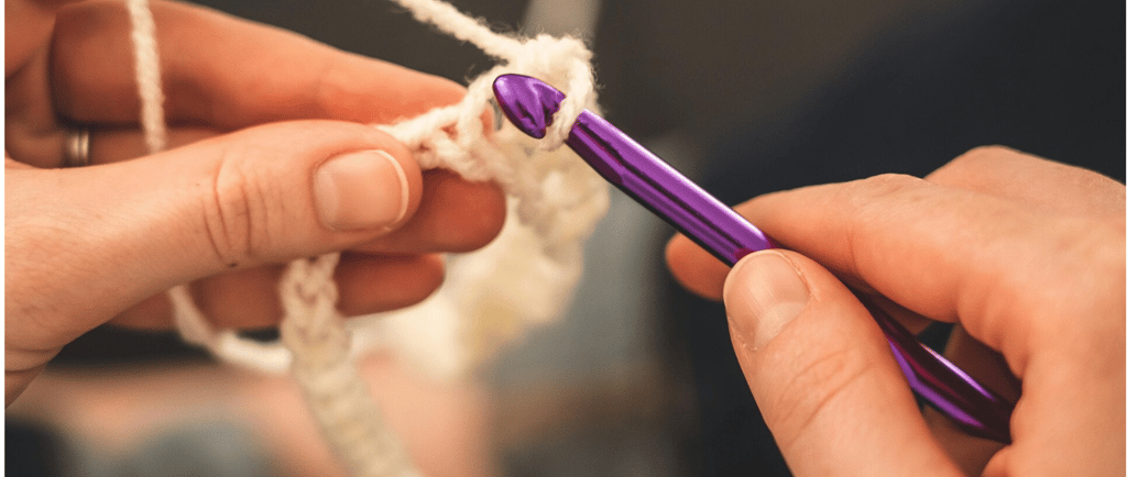 une personne crochète un morceau de laine avec une paire de mains
