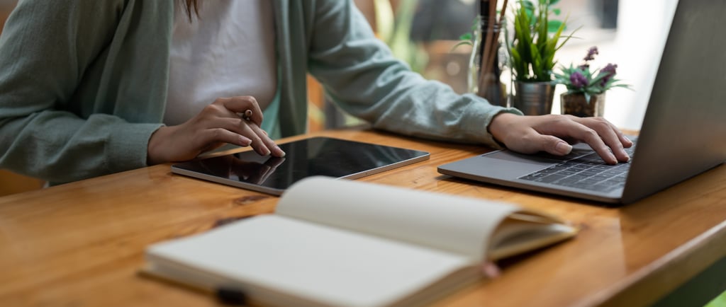 "Speech therapy professional using tablet and laptop for virtual session planning with notebook on d