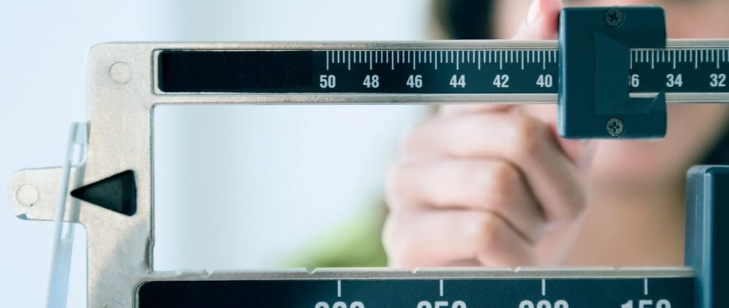 A woman adjusts the sliding weights on a professional physician beam scale to measure body weight.