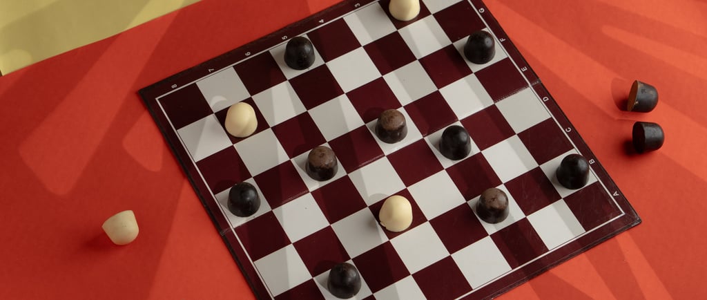 A game of checkers played with dark and white chocowell chocolates on a classic red and white board.