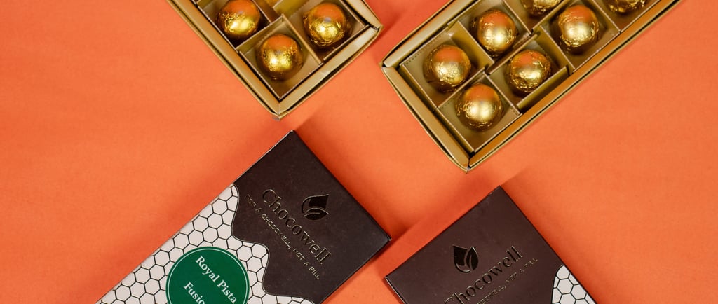 Gourmet gold foil-wrapped chocolate truffles in gift boxes on an orange background.