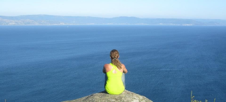 a woman sitting on a rock in front of a body of water