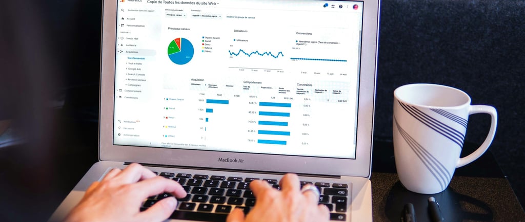 Person analyzing Google Analytics data on a laptop with a cup of coffee and pens nearby.